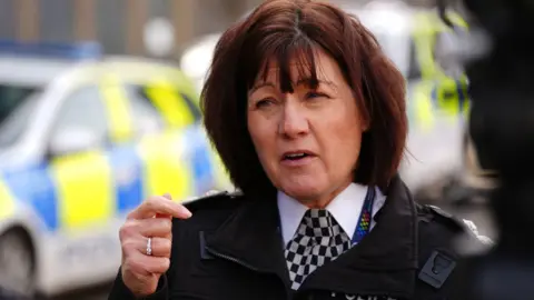 Jo Farrell, a woman with reddish-brown hair in a Police Scotland uniform, is standing talking to someone outside. A police car is in the bakcground.