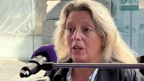 A woman with blonde hair behind a purple microphone.