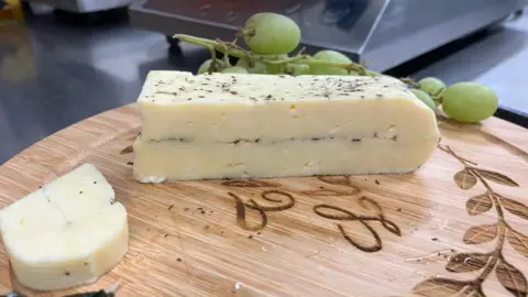 A slab of cheese on a board, with green grapes next to it