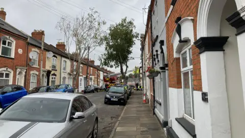 Pete Cooper/ BBC A fire crew up a ladder tackling a fire in a terraced house