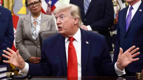 US President Donald Trump speaking in the Oval Office surrounded by people listening