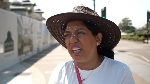 Shaun Whitmore/BBC Gulshan Glavin standing outside in Great Yarmouth. She is wearing a white T-shirt and a brown straw hat on her head.