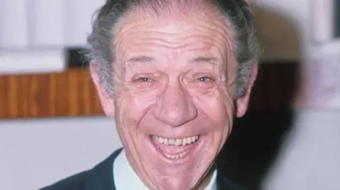 Sid James, who has grey hair, smiling broadly