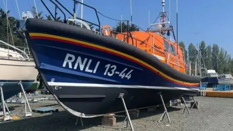 The George and Frances Phelon lifeboat in bright orange and navy blue, stored on dry land.