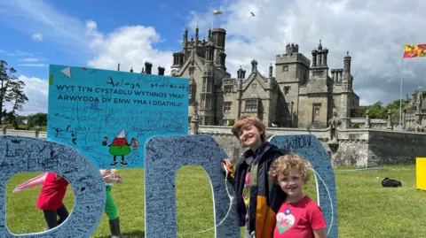 Thomas and Toby stand by large blue letters which are covered in people's names and signatures. Margam Castle can be seen in the background.