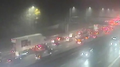 Traffic England A mix of cars and HGVs can be seen queuing. It is dark and the lights from the cars are the main source of light.