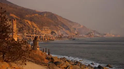 Smoke rises from burnt-down beachfront homes along the road to Malibu, as powerful winds fueling devastating wildfires in the Los Angeles area force people to evacuate.