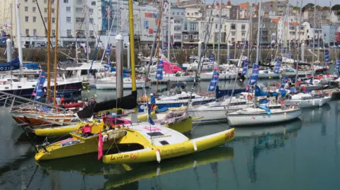 The marina is full of small yachts, many of which are decorated with bunting and flags.