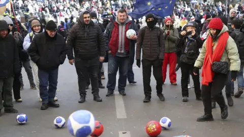 EPA Protesters outside Georgia's Parliament, wearing jackets and hats, held red cards and kicked footballs, with one waving an EU flag 