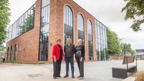 Chesterfield Borough Council A man flanked by two women pose in front of a new brick and glass building.