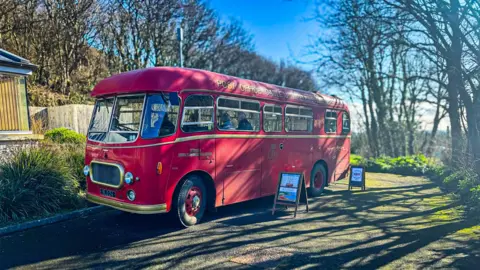 Cornwall Council A red 1950s bus with gold bumpers and trim. 