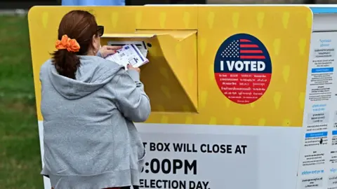 Getty A woman stands at a yellow ballot drop box in California, which has the words 'I voted' displayed on the side.