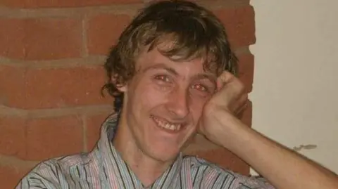 Staffordshire Police A man with messy, dark blonde/light brown hair is looking towards the camera and smiling