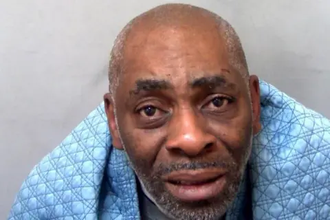 Essex Police A police station photograph of a man with a blue blanket over his shoulders. He looks at the camera.
