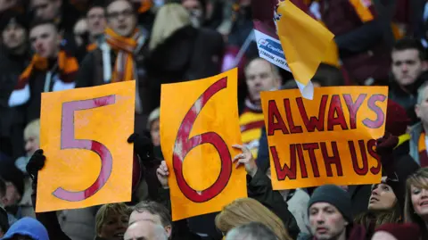 Getty Images Football supporters hold up claret-and-amber paper signs bearing the words: "56, always with us".