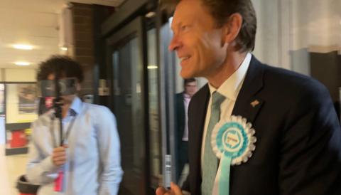 Richard Tice wearing a rosette entering the sports centre where the count was taking place