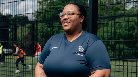 Morgane Bigault / Comic Relief A woman wearing glasses and a blue top smiles