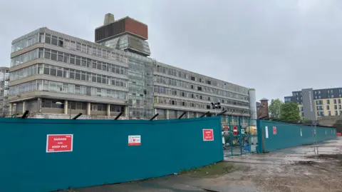 Owen Sennitt/BBC A grey Brutalist office block from the late 1960s can be seen with hoardings surrounding it on a grey day 