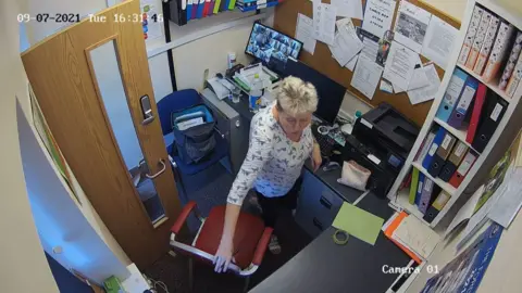 Dudley Metropolitan Borough Council A CCTV image of a woman in an office. She is standing up with her hand on a red office chair.
