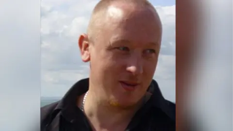 Eugene Scardifield Close up of a man with a shaved head, wearing a polo shirt and silver chain around his neck