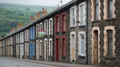 Getty Images A row of terraced homes on a sloped street. They all have stone facades, but have different coloured window sills and porches. 