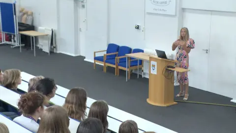 Deputy Head Emma Browne standing in front of a lectern in a lecture theatre talking to students about misogyny in the workplace