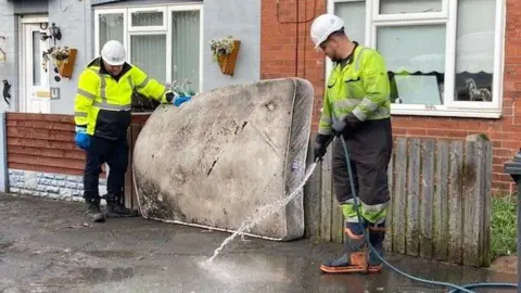 Two workers clean a path outside with a flooded mattress 