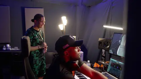 AJ in the studio wearing a green and black tracksuit, with her music producer, Winter.
