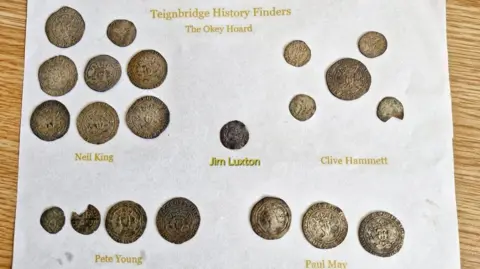 The coins arranged on a white background, with text labelling different sections. The coins are divided into groups attributed to different individuals. Each individual's name is printed in gold text below their respective section of coins. The coins appear to be of various sizes.