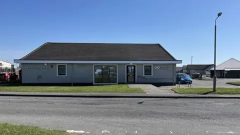 The bank is long low building with three windows and a door at its front.