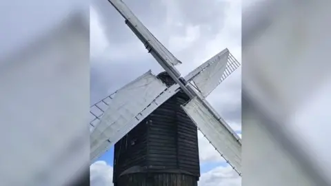 The windmill has a wooden frame which has been painted black. The rotating arms have been painted white and now have material wrapped around them to make them rotate in the wind.