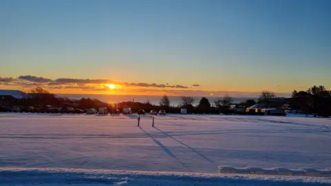 Snow along a flat piece of ground at sunrise, you can see the sea in the background.
