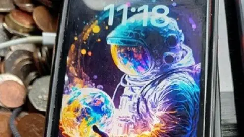 Merseyside Police Close-up of a mobile phone with an illustration of an astronaut in space, holding a planet in their hands