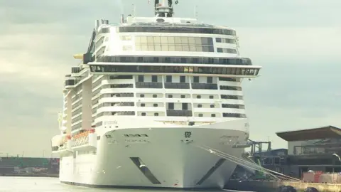 White cruise ship berthed with ropes to its left side onto the docks.