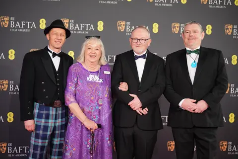 James Manning/PA Wire Three men in black dinner suites and a woman in a purple dress stand before a display board