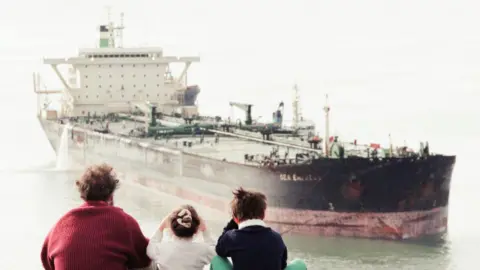 Mirrorpix A man and two children watch as the Sea Empress is towed to a jetty 