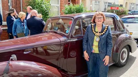 Leamington Town Council Sarah Boad stands next to a Rolls-Royce. She is wearing a dark blue trouser suit and green top and her chains of office around her neck. 