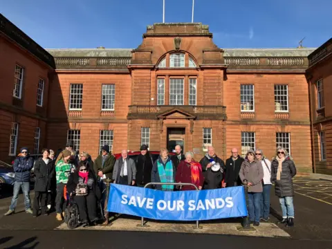 A group of protesters with a "Save Our Sands" banner outside the council headquarters - an imposing sandstone building - in Dumfries