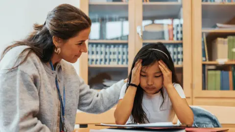 Getty Images Female counselor consoling girl sitting with head in hands at a school