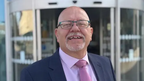 LDRS Doncaster councillor Glyn Jones wearing a suit, pink tie, mauve shirt and with a bald head, smiling widely