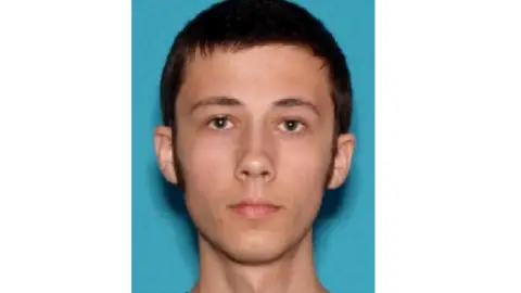 FBI A young man is shown against a blue backdrop in a police mugshot image.