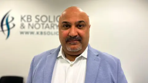 A man wearing a suit inside a solictors' office looking into the camera