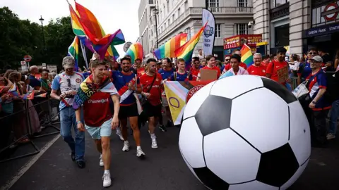 Getty Images A group of men in football kit carrying flags walk in the parade, with an oversized football.