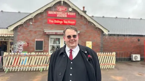 Andrew Mould, events manager, is standing outside The Sidings tea room at Brownhills West Station.