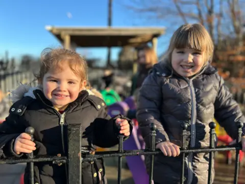 Two children who attend the nursery. They are leaning on a fence and smiling. 