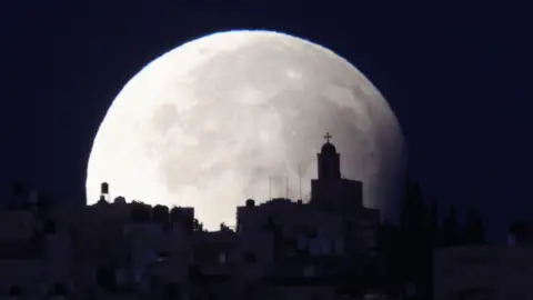 EPA A supermoon with a partial lunar eclipse sets over the old city of Jerusalem, 18 September 2024.