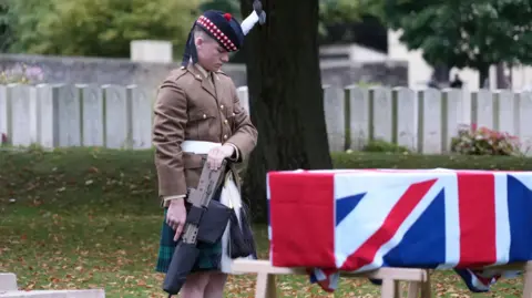 Soldier with head bowed at coffin draped in Union Jack 