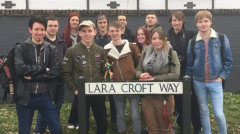 Amy Dyson A group of fans stood together near a road sign that says "Lara Croft Way"