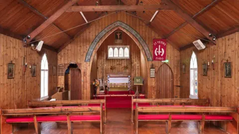 Historic England The inside of a small church with pews with red cushions, an alter and small windows