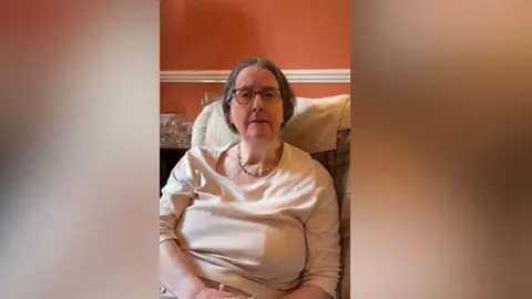 Fr Christopher Woods Dr Joy Tetley looking at the camera while speaking to Fr Christopher Woods a her home.